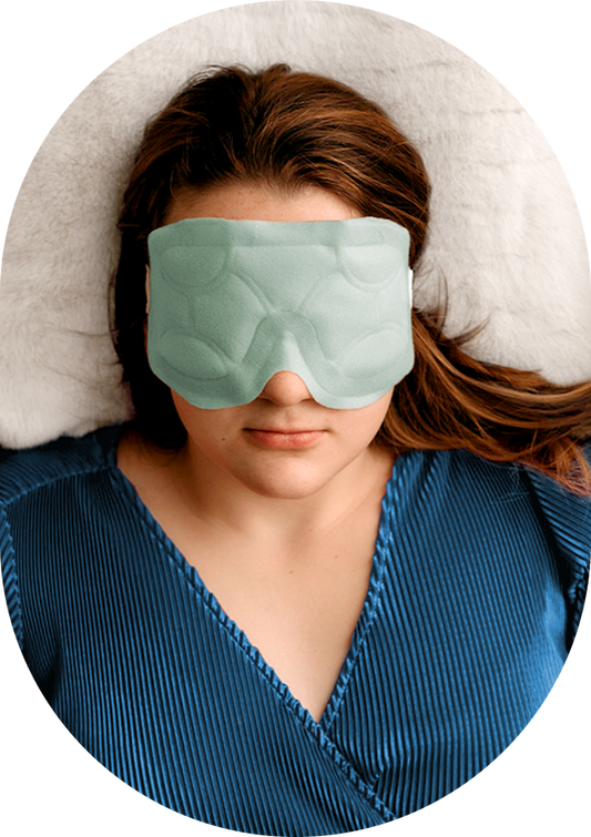 Person wearing a green sleep mask with a white pillow in the background
